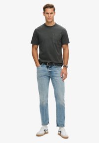 Korte mouwen antraciet t-shirt met een borstzak, gecombineerd met lichtblauwe spijkerbroek en witte sneakers met zwarte accenten.