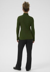 Ribota olīvzaļā turtlenecka džemperis, kas apvienots ar melniem izpletņbiksēm, ar pieguļošu siluetu un garām piedurknēm. Gluda tekstūra, minimāls noformējums.