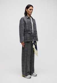 Gray patterned denim jacket with matching wide-leg trousers. White top underneath, complemented by a patterned scarf and silver athletic shoes.