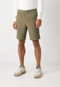 Olive green shorts with an elastic waistband, featuring a smooth fabric texture and a relaxed fit, paired with light-colored sneakers.