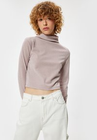 Lichtroze cropped turtleneck gemaakt van ribbelstof, gecombineerd met hoge witte jeans. Heeft lange mouwen en een getailleerd ontwerp.