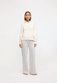 White hooded sweatshirt with a front pocket, paired with loose, light gray, wide-leg pants in soft fabric. Plain design, no patterns.