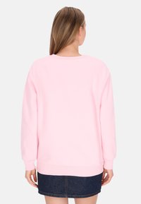 Sudadera rosa con cuello y puños acanalados. Tejido suave y ajuste cómodo, combinada con una falda de mezclilla oscura. Vista trasera, sin patrones ni adornos.