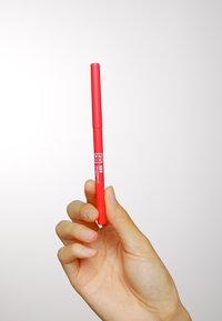 Un marqueur rouge tenu dans une main, avec un corps cylindrique et une texture lisse et mate. L'étiquette affiche "334" et d'autres détails du produit.