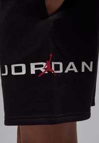 Schwarze Baumwollshorts mit weißem "JORDAN"-Logo und einer roten Silhouettengrafik. Das Design ist schlicht mit einem geraden Saum und seitlichen Taschen.