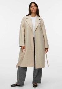 Beige wollen blend jas met een opstaande kraag, brede mouwen en een ceintuur in de taille, gecombineerd met donkergrijze wijde broekspijpen. Soepele textuur.