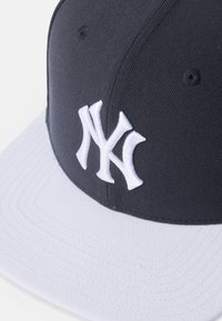 Ciemnoniebieska czapka z białym daszkiem, na froncie z uniesionym haftowanym białym logo "NY".