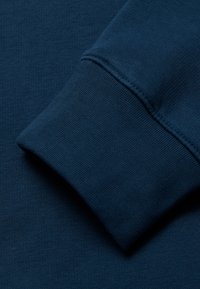 Primer plano de tela de sudadera azul oscuro, que presenta un puño acanalado con una textura suave y detalles de costura sutiles.