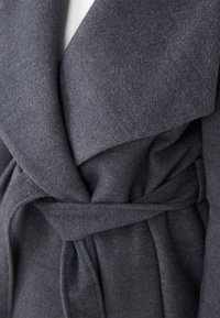 Grijze wollen wikkeljas met een brede kraag, een ceintuur in de taille en een zachte, gestructureerde stof. Zichtbare plooien en een gestructureerd silhouet.