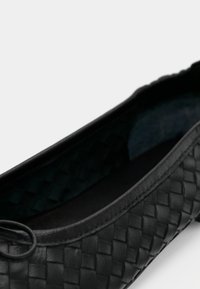 Μαύρο πλεκτό δερμάτινο μπαλαρίνα με στρογγυλεμένη μύτη, λεία εσωτερική επένδυση και μινιμαλιστικό σχεδιασμό, με μικρή λεπτομέρεια δακτυλίου στο πλάι.