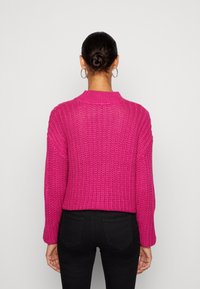 Fuksianvärinen neulottu neulepaita, jossa on pyöreä pääntie ja pitkät hihat. Neuleessa on teksturoitu kuvio, lyhyt malli ja resorit hihansuissa.