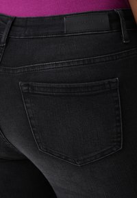 Black denim jeans with a smooth texture, featuring a rear pocket and a rectangular label reading "ONLY CARMAKOMA."