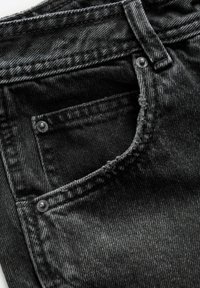 Gros plan sur un jean en denim noir montrant la poche avant, une petite poche à monnaie, une boucle de ceinture et des rivets métalliques sur un tissu texturé.