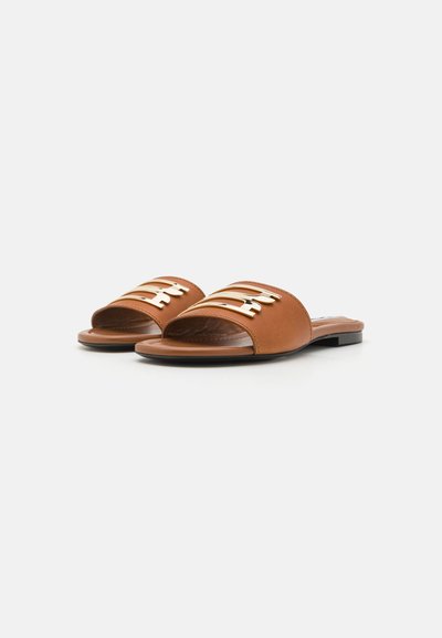 Sandales à glisser en faux cuir marron avec un bout ouvert, présentant trois accents en métal doré horizontal sur la sangle supérieure. Design à semelle plate.