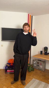 Black hoodie with a kangaroo pocket, loose-fitting black cargo pants, and brown slip-on shoes. Standing in a modern room with decor elements.