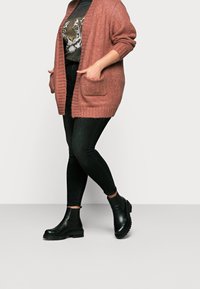 Rusty pink knitted cardigan with open front and two pockets, paired with black skinny jeans and black ankle boots with a textured sole.