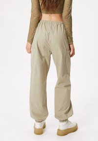 Pantalones cargo de color beige claro, fabricados con material suave, que presentan un corte holgado, cintura elástica y puños elásticos. Incluyen bolsillos laterales para mayor utilidad.