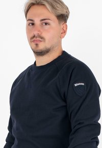 Navyblauwe sweatshirt van katoen met een ronde halslijn en lange mouwen. Heeft een gestructureerde patch op de linkerschouder met het label "Blauer".