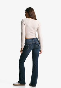 Light pink cropped sweater with ribbed hem, paired with dark blue flared jeans featuring embroidered back pockets and white sneakers.