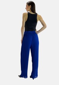 Zwarte tanktop en blauwe geplooide broek met wijd uitlopende pijpen en een elastische tailleband, voorzien van verticale plooien en een lichtgewicht stof.