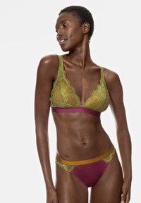 Grön spets-bh med blommönster, med en vinröd rem. Matchande vinröda trosor med grön spetskant och elastiskt midjeband.