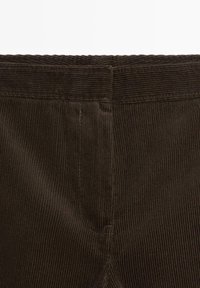 Bruin corduroy stof met verticale ribbels, voorzien van een tailleband en gestikte naden. De textuur is zacht met een ribbelpatroon.