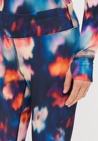 Barvite atletske legice z večtonskim cvetličnim vzorcem v modri, oranžni in roza barvi; teksturirano blago; vključujejo prilegajoč pas in dodatke.