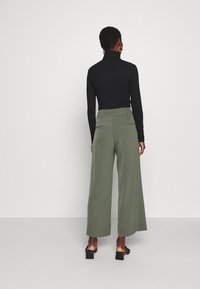 Musta poolikaulus paita yhdistettynä leveälahkeisiin oliivinvihreisiin housuihin, joissa on kaksi takataskua, sileä pinta ja rento istuvuus. Mustat korokepohjaiset sandaalit.