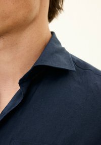 Camicia blu navy in lino, caratterizzata da un colletto strutturato, una trama sottile e una patta con una singola tasca sul petto.