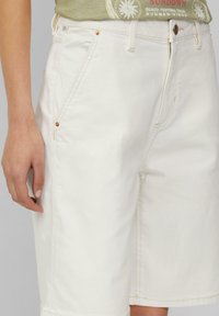 Shorts en denim blanc avec une coupe droite, dotés d'accents en métal allié cuivre, de cinq poches et de coutures visibles.