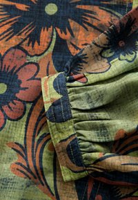 Bloemrijk stof met een patroon in donkergroen, oranje en blauw. Close-up van een gathered mouwmanchet met zichtbare stiksels.