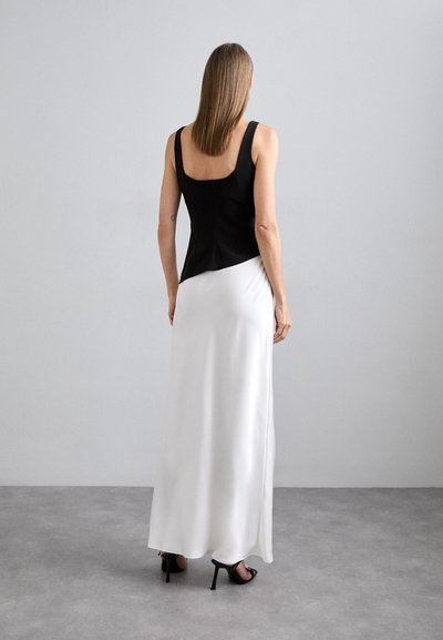 Black sleeveless top with a square neckline paired with a flowing white satin skirt; features a fitted bodice and smooth texture. High-heeled shoes visible.