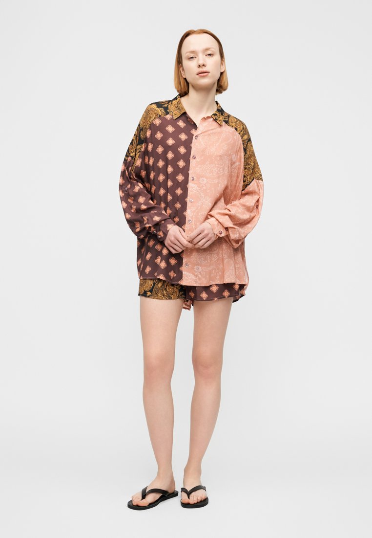 Chemise à motifs multiples à manches longues, design divisé en rose et marron, avec des boutons. Associée à un short assorti et des tongs.