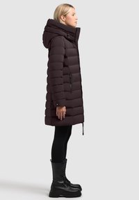 Cappotto piumino nero con colletto alto e cappuccio, caratterizzato da un design a quadri orizzontali, tasche con zip e un taglio fino al ginocchio, abbinato a stivali alti fino al ginocchio.
