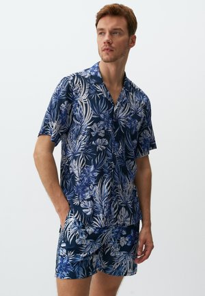 Kurzärmeliges Hemd und Shorts-Set in Dunkelblau mit weißen und hellblauen tropischen Blumenmustern. Leichter Stoff, entspannte Passform.