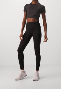 Czarna, krótka koszulka sportowa i czarne legginsy w wysokim stanie. Gładka tekstura z delikatnymi paskami. Połączone z białymi sneakersami.