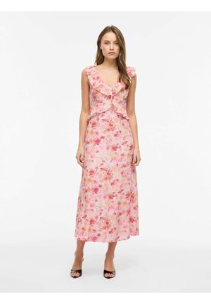 Kvinde iført ærmeløs lyserød blomstret midikjole med flæset V-hals og sorte åbne hæle, stående mod hvid baggrund.