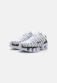 Baskets blanches de sport avec une tige en mesh, des accents gris et un design de semelle ondulée distinctif comportant plusieurs colonnes de coussinage.