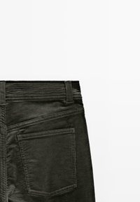 Pantaloni in corduroy di colore verde scuro, caratterizzati da righe testurizzate, una vita piatta e una tasca posteriore con un semplice contorno cucito.