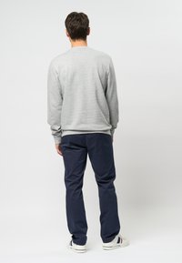 Hanorac gri cu mâneci lungi, croială lejeră, purtat cu pantaloni bleumarin. Modelul poartă adidași albi cu accente de culoare.