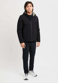 Giacca nera con cappuccio a zip, dotata di un cappuccio foderato in grigio, abbinata a pantaloni neri e scarpe grigie. Tessuto liscio, vestibilità moderna.