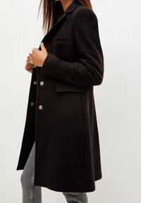 Svart ullblandad kappa med skräddarsydd design, slagkragar, dubbelknäppta knappar och sidoficka, med en mjuk textur.