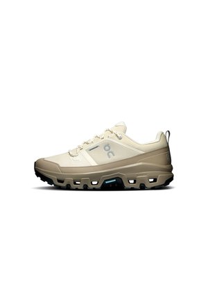 Beige and tan lace-up athletic shoe with thick, rugged black sole designed for outdoor trail running or hiking.