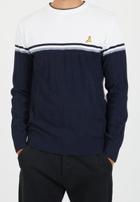 Granatowy sweter z dzianiny z białymi i szarymi poziomymi paskami. Żebrowana struktura, okrągły dekolt i małe żółte logo na klatce piersiowej.