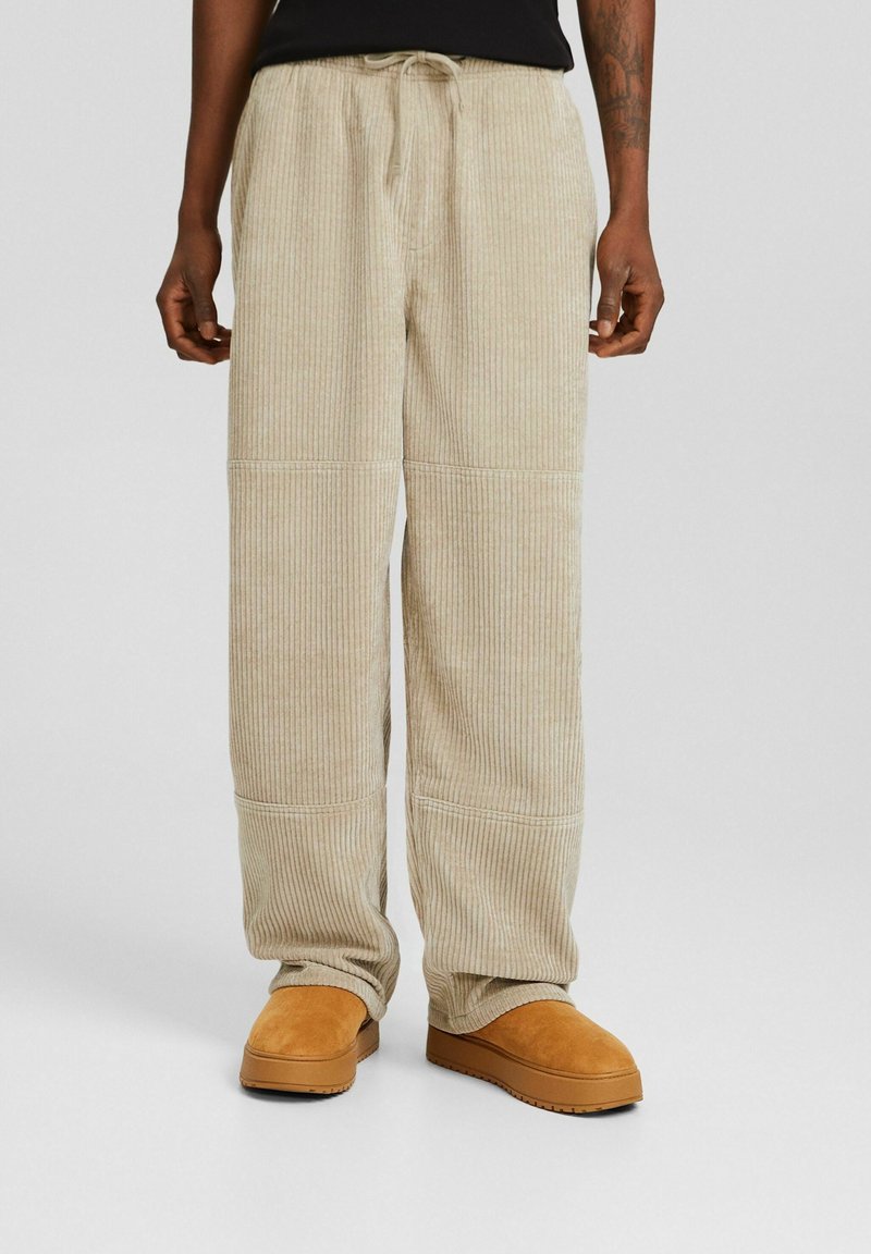 Beige corduroy broek met een losse pasvorm, voorzien van verticale strepen, een elastische tailleband met trekkoord en zichtbare stikdetails.