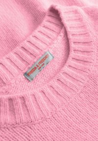 Różowy, dziany sweter z prążkowanym dekoltem; posiada metkę z napisem "FRIEDA & FREDDIES" w srebrnym kolorze z czerwonymi akcentami. Miękka tekstura.