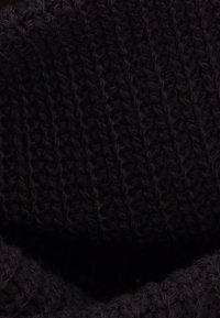 Gros plan d’un tissu tricoté noir avec des motifs de points côtelés et tressés visibles.