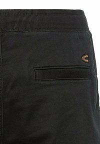 Schwarze Baumwollhose mit geripptem Bund, ausgestattet mit einer aufgesetzten Tasche und einem kleinen, in Braun gestickten Logo. Glatte Stoffstruktur.