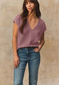 Top a manica corta con scollatura a V in tessuto lavanda testurizzato abbinato a jeans in denim blu, con vita aderente e leggero effetto usurato.