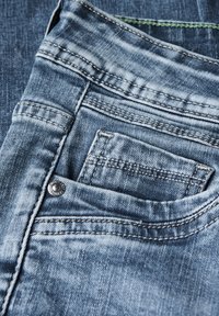 Jeans i ljusblått denim med en blekt textur. Har framträdande sömmar, en liten framficka och en metallisk knappdetalj.